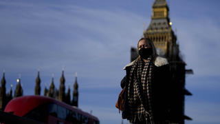 09.12.2021, Großbritannien, London: Eine Frau mit Mund-Nasen-Schutz überquert die Westminster Bridge. Premierminister Johnson kündigte als Reaktion auf steigenden Neuinfektionen und die Omikron-Variante des Coronavirus neue Corona-Beschränkungen an. Foto: Frank Augstein/AP/dpa +++ dpa-Bildfunk +++