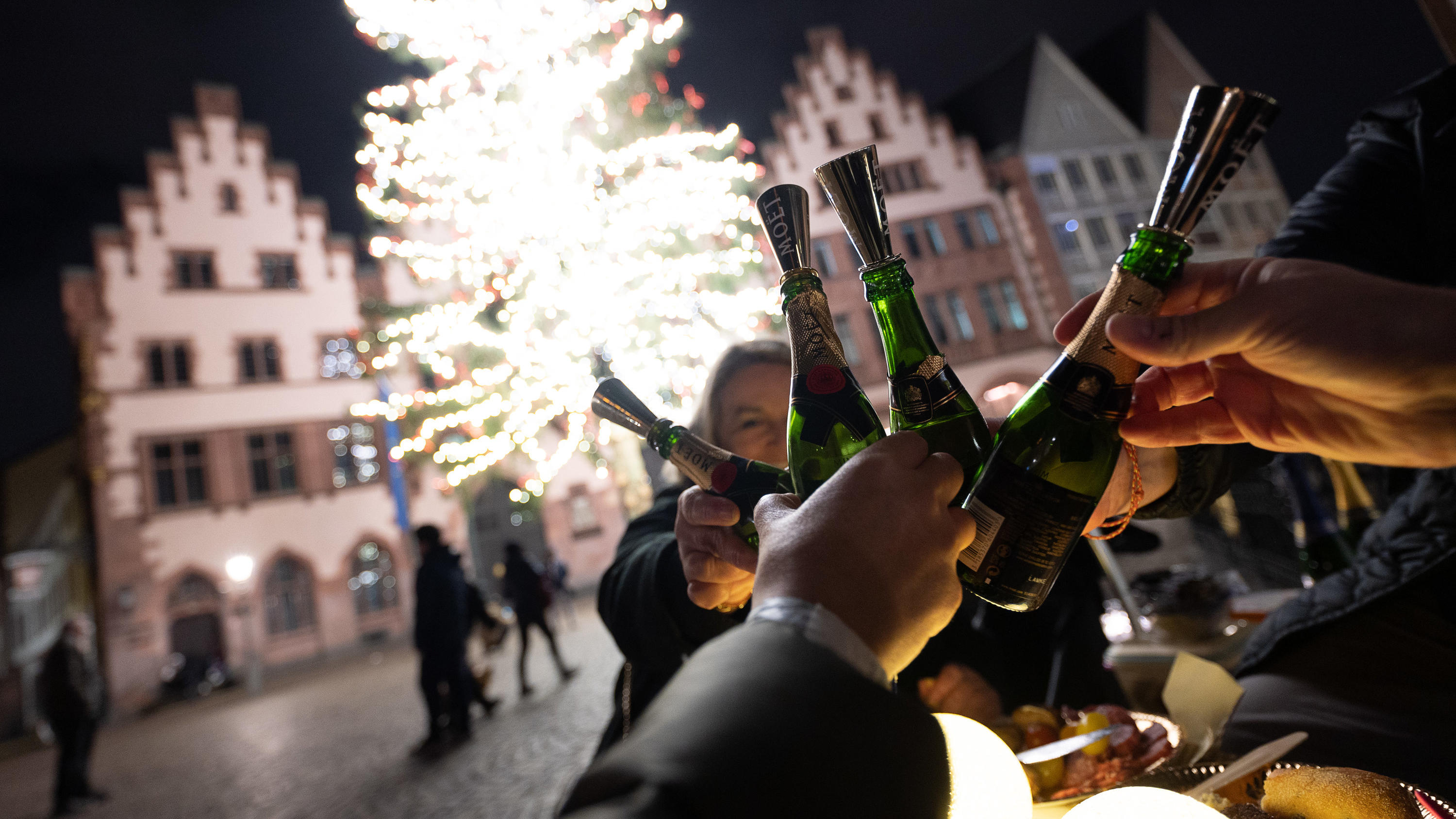 31.12.2021, Hessen, Frankfurt/Main: Menschen stoßen an einem Tisch auf dem Römer mit Champagner an. Aufgrund der Corona-Maßnahmen haben sich die Anstoßenden dazu entschieden an der frischen Luft ins Neue Jahr zu feiern. Vorspeise gab es an der Alten 