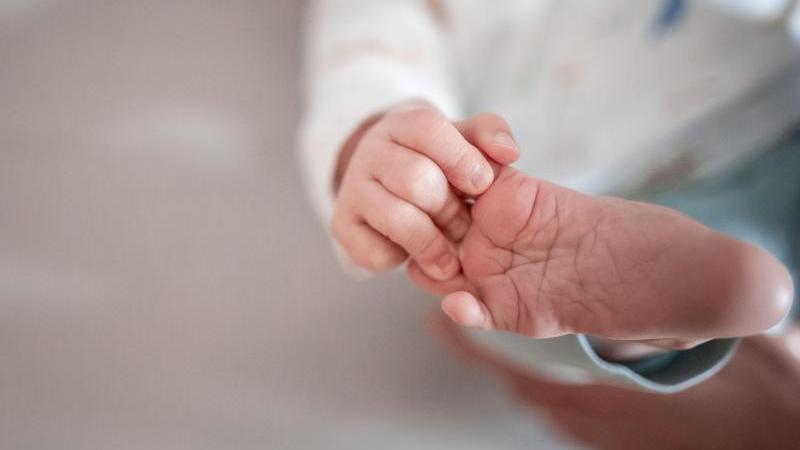 Ein Baby greift mit den Fingern nach seinem Fuß. Symbolfoto: Fabian Strauch/dpa/Illustration