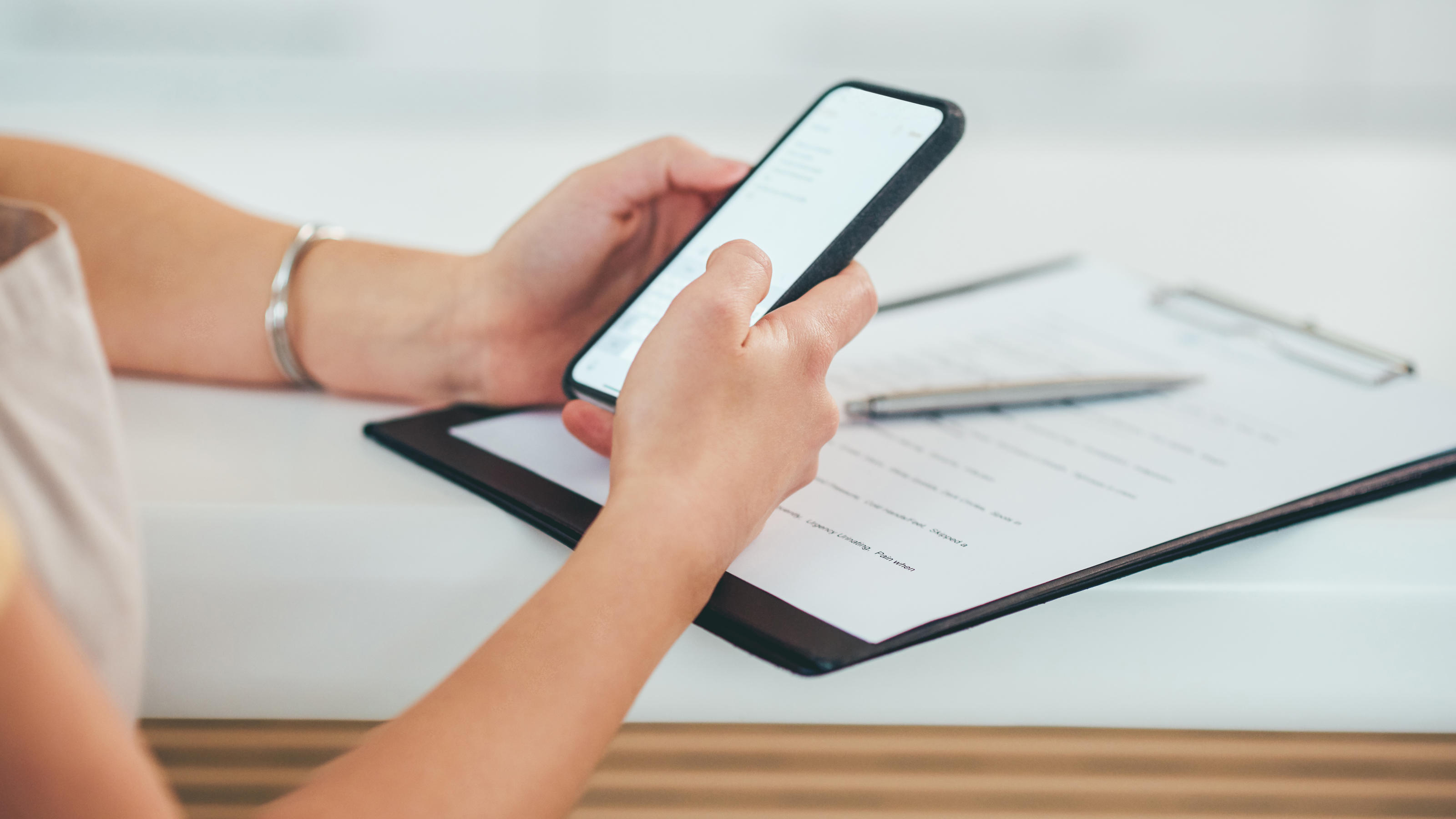 Eine Frau sitzt am Schreibtisch und hält ein Smartphone in den Händen.