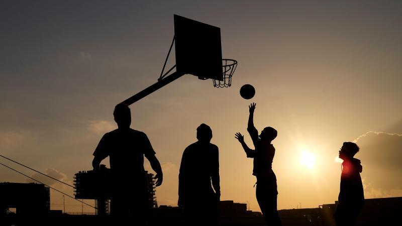 Jugendliche spielen in der Abendsonne Basketball. Foto: Oliver Berg/dpa/Symbolbild