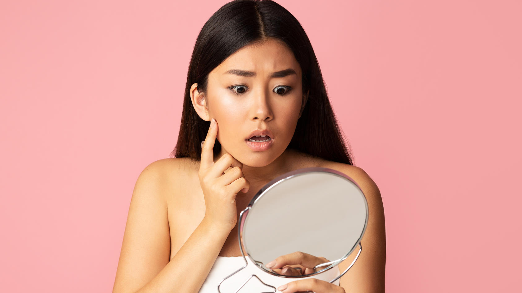 Botox-Creme: Frau schaut sich schockiert im Spiegel an.