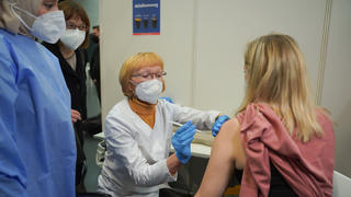 18.01.2022, Brandenburg, Potsdam: Ursula Nonnemacher (2.v.l, Bündnis90/Die Grünen), Brandenburgs Gesundheitsministerin, sieht dabei zu, wie die Apothekerin Barbara Oberüber (2.v.r) einer Frau in der Impfstelle Metropolishalle eine Corona-Impfung erklärt, während die Ärztin Bushra Malik ihr beratend zur Seite steht. In Brandenburg starten in dieser Woche die Schulungen von Apothekerinnen und Apotheker zur Corona-Impfung. Foto: Joerg Carstensen/dpa +++ dpa-Bildfunk +++