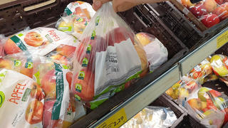 Ein Kunde hat einen mit Obst, Gemuese befuellten Plastikbeutel, Beutel, Knotenbeutel, Faltenbeutel an der Obst- und Gemuesetheke iim Supermarkt Edeka in seiner Hand, Finger.