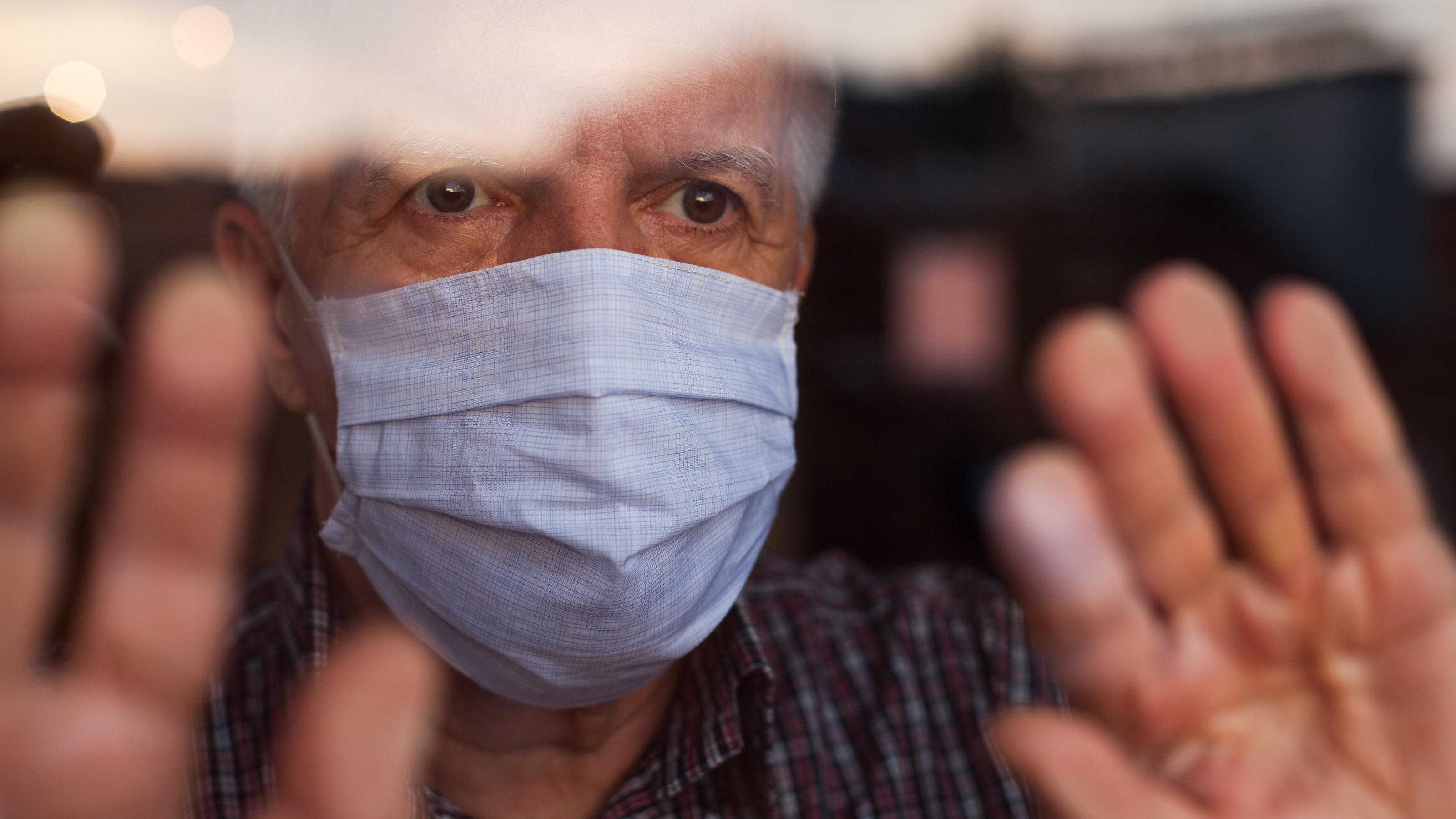 Ein älterer Mann trägt Mund-Nasenschutzmaske und scheint sich in Isolation zu befinden.