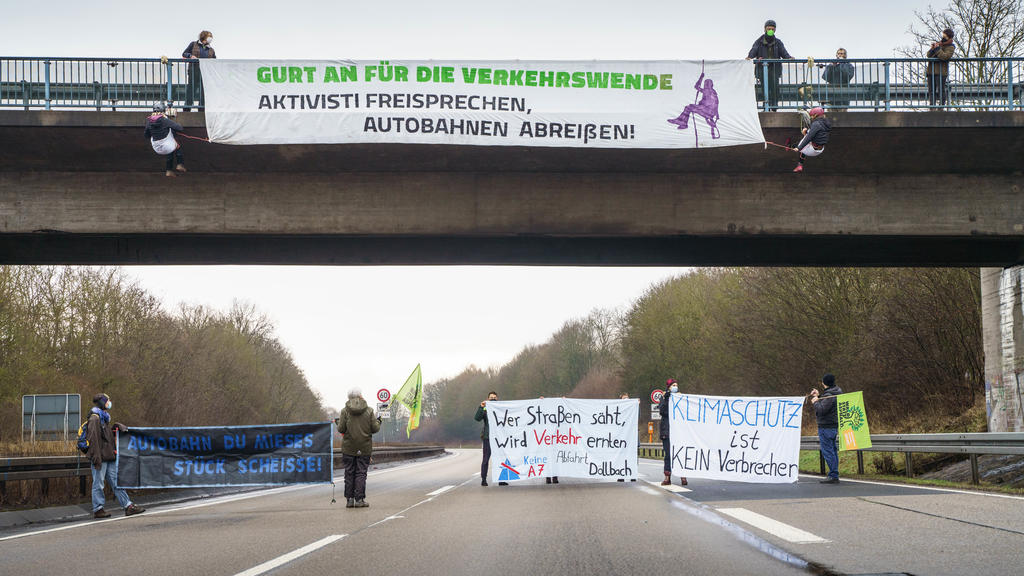 23.01.2022, Hessen, Künzell: Aktivisten mit Transparenten stehen auf der gesperrten Fahrbahn der Autobahn A7 am Rande von Künzell bei Fulda, während oben an einer Bücke eine genehmigte Abseilaktion stattfindet. Mit der Aktion soll für eine echte Verk