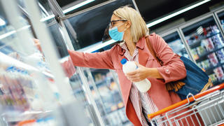Junge Frau mit Maske kauft Milch im Supermarkt ein.