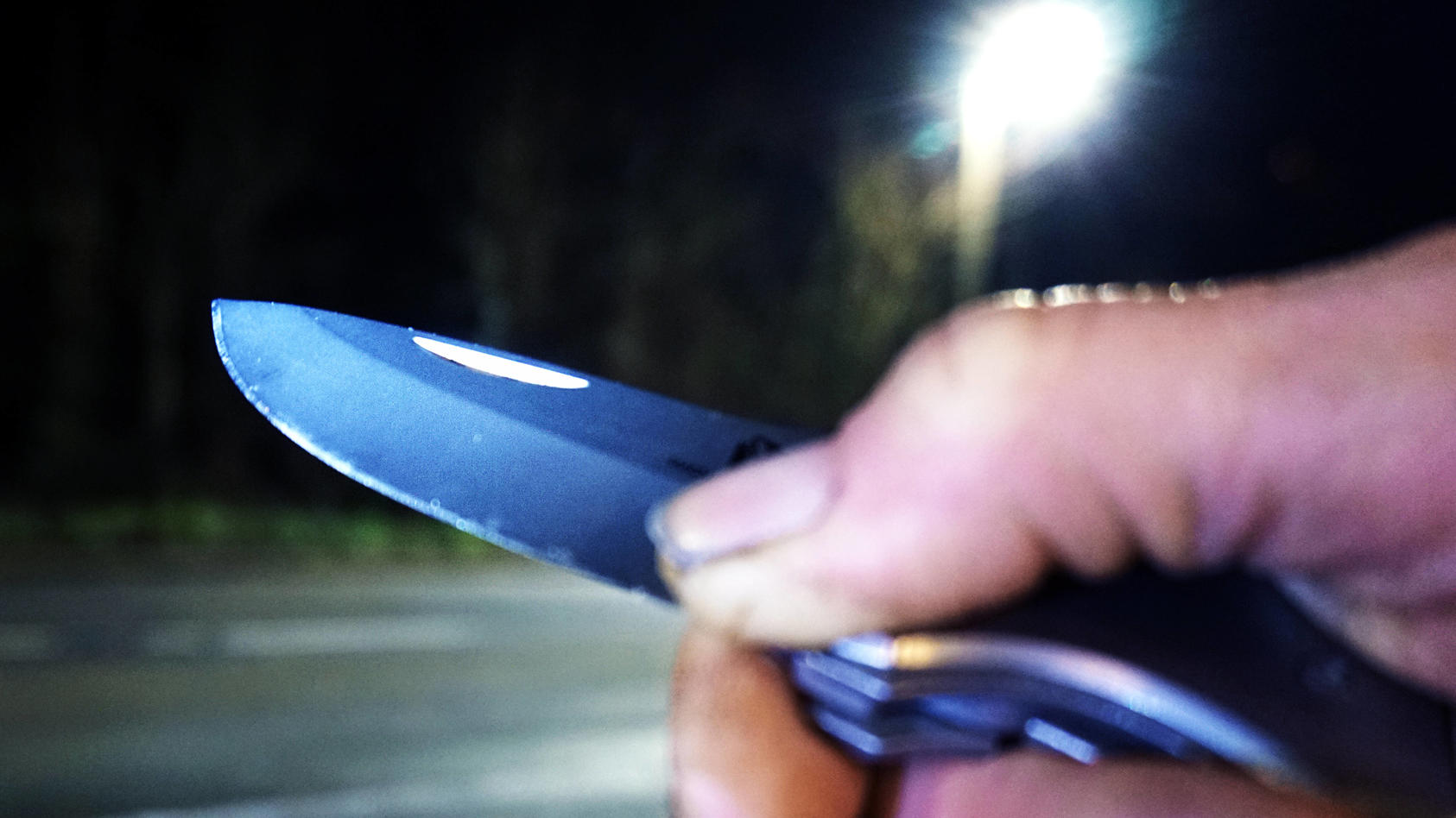 Kriminalität, Raub und Überfall / Raubüberfall - Symbolbilder Angriff mit Messer / Messerangriff - Symbolbilder .Messer als Kampfmittel und Waffe Eine Person hält bei Dunkelheit an einer Straße ein Messer in der Hand. *** Knife as a combat device and
