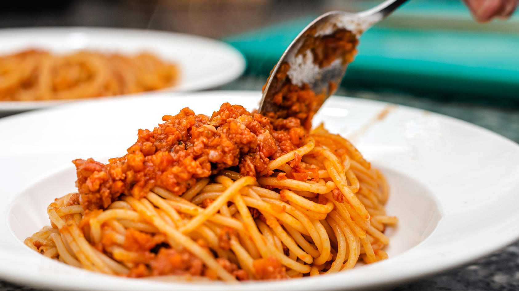 Koch richtet Spaghetti Bolognese auf Teller an