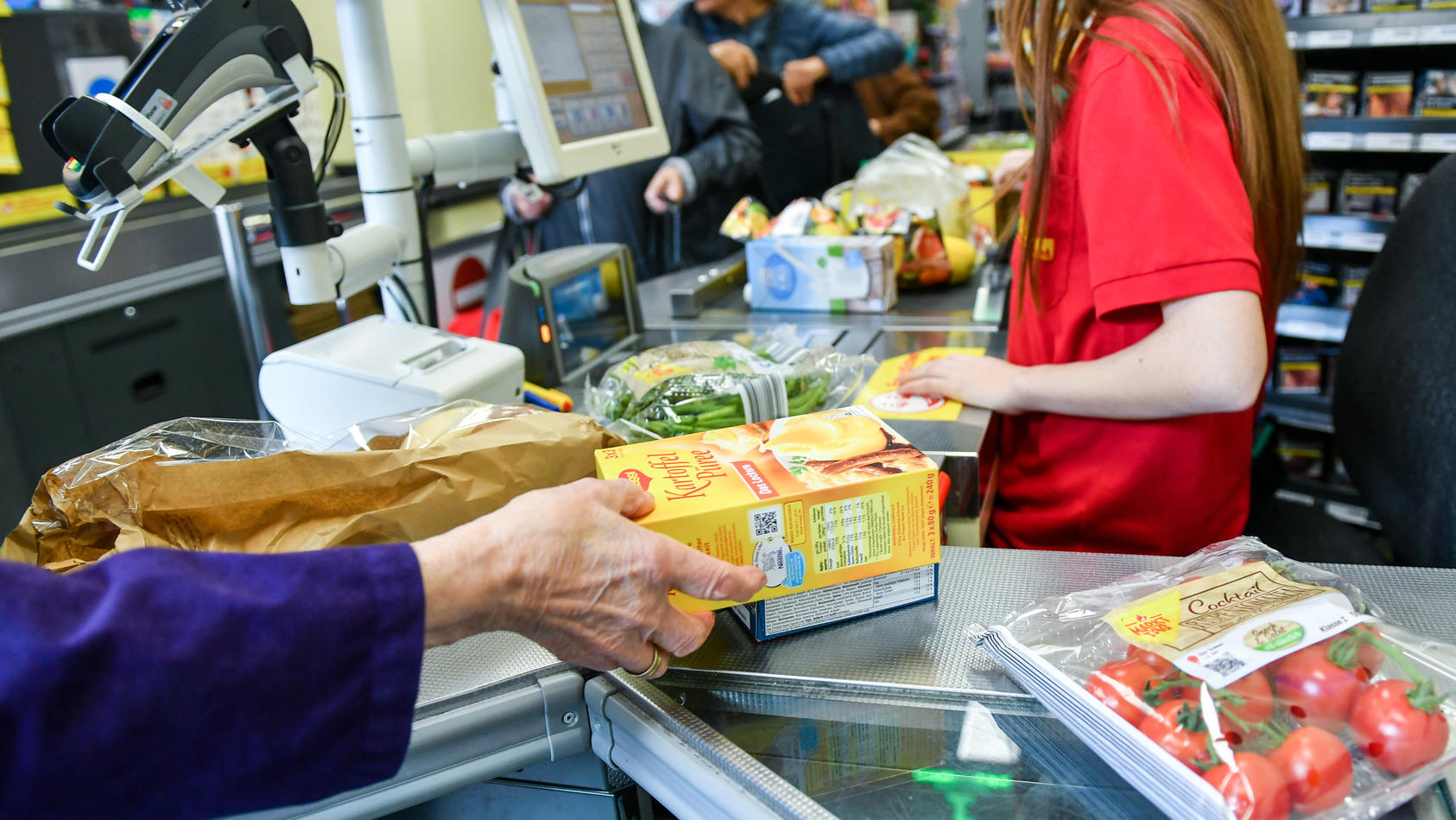 ARCHIV - 18.09.2019, Berlin: Eine Kundin nimmt in einem Supermarkt Waren vom Band an der Kasse, nachdem eine Kassiererin die Waren gescannt hat. Deutsche Verbraucher und Unternehmen müssen sich nach Einschätzung des Ifo-Instituts auf weitere Preiserh