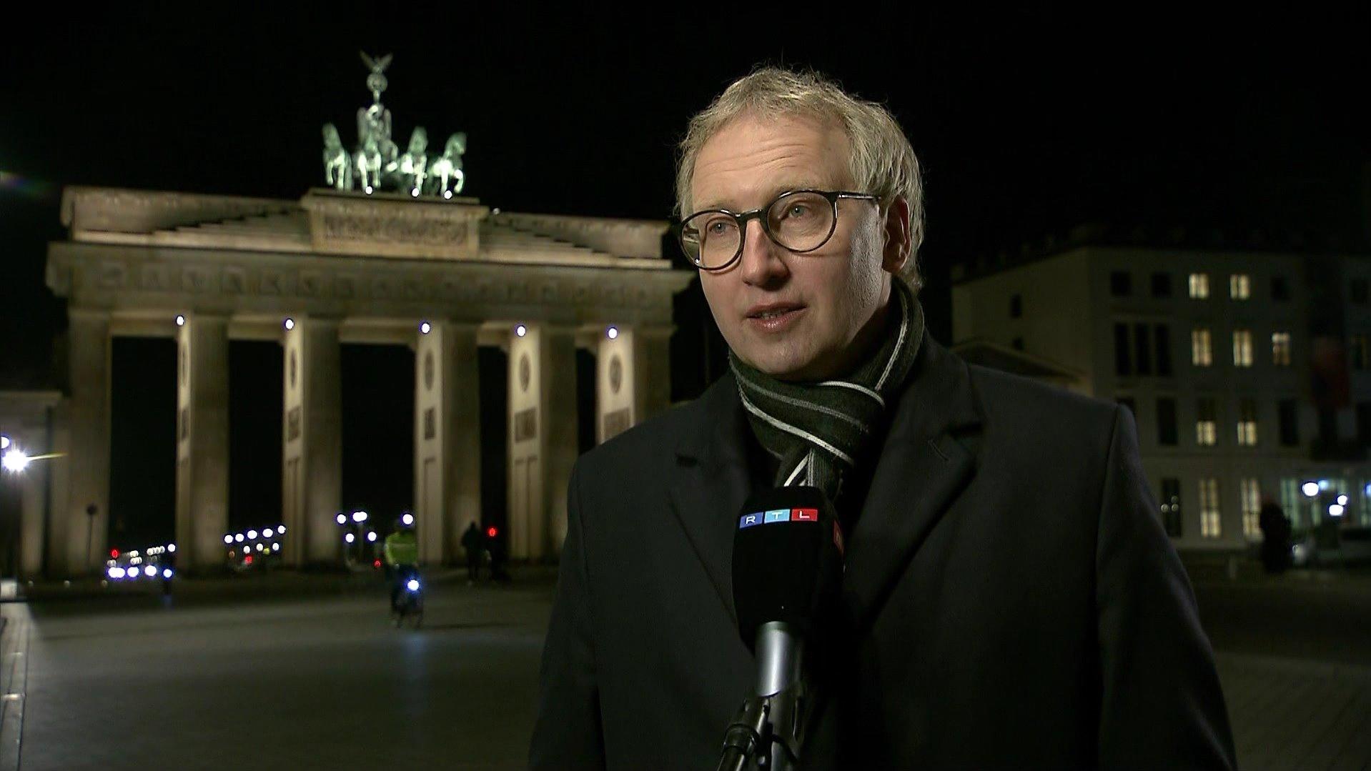Johannes Varwick steht nach Sonnenuntergang vor dem beleuchteten Brandenburger Tor in Berlin.