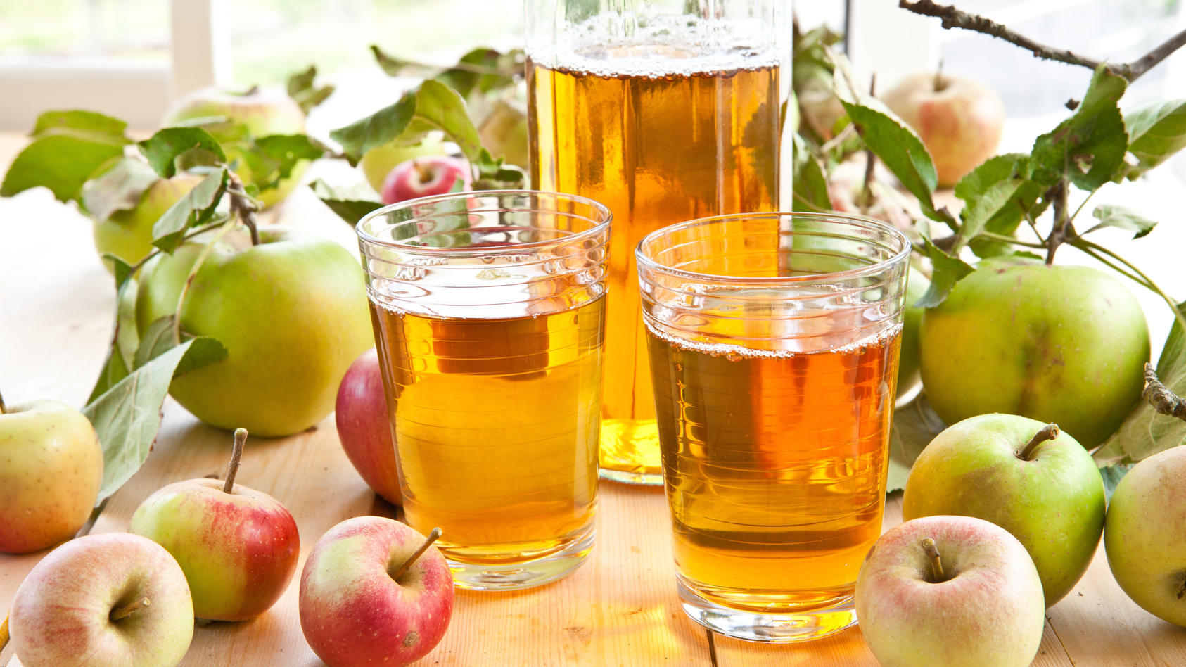 Apfelsaft in Krug und Gläsern, umgeben von Äpfeln