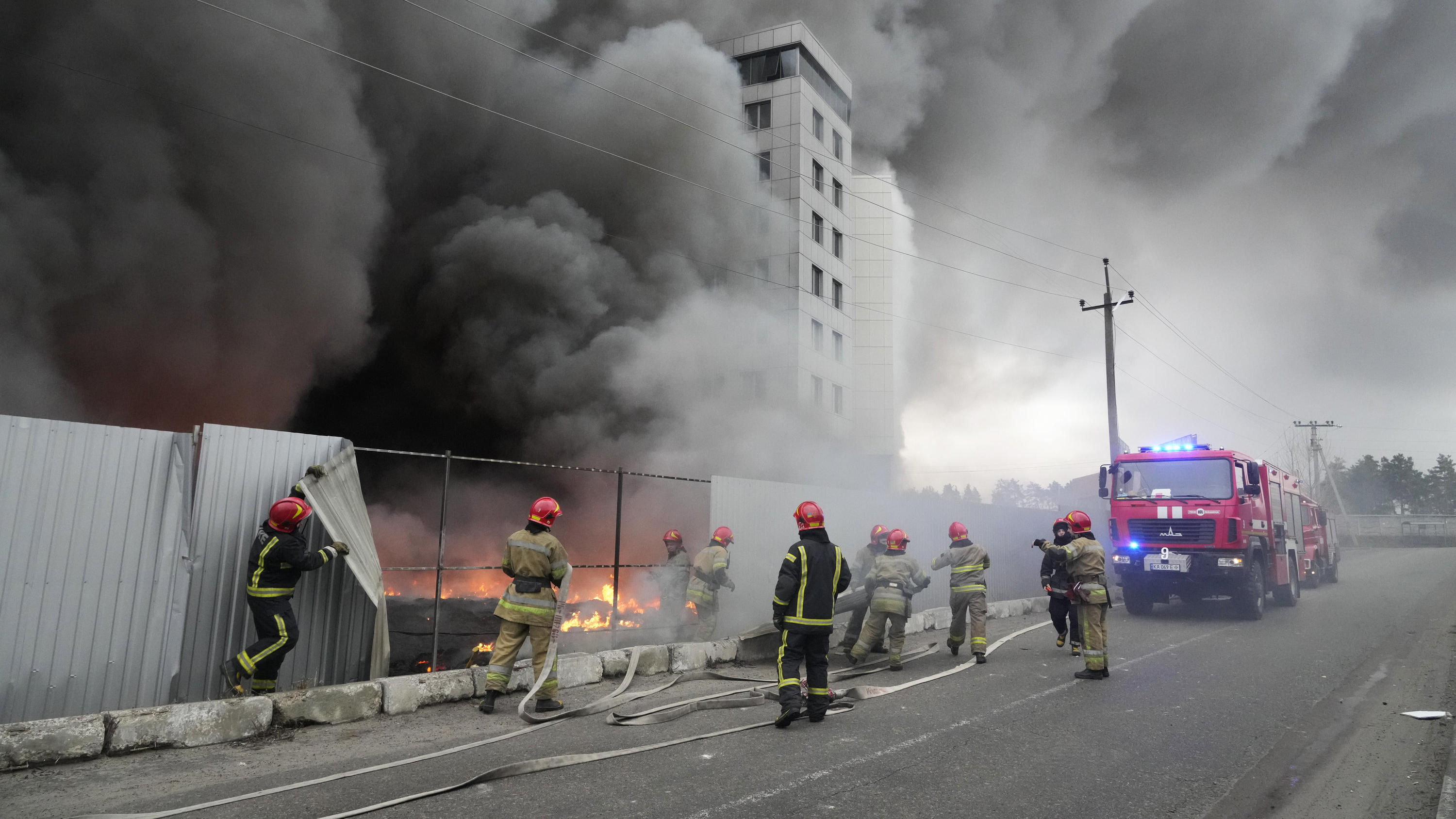 Einsatzkräfte der Feuerwehr stehen vor einem ukrainischen Logistikzentrum, dass nach Beschuss in Brand geraten ist. 