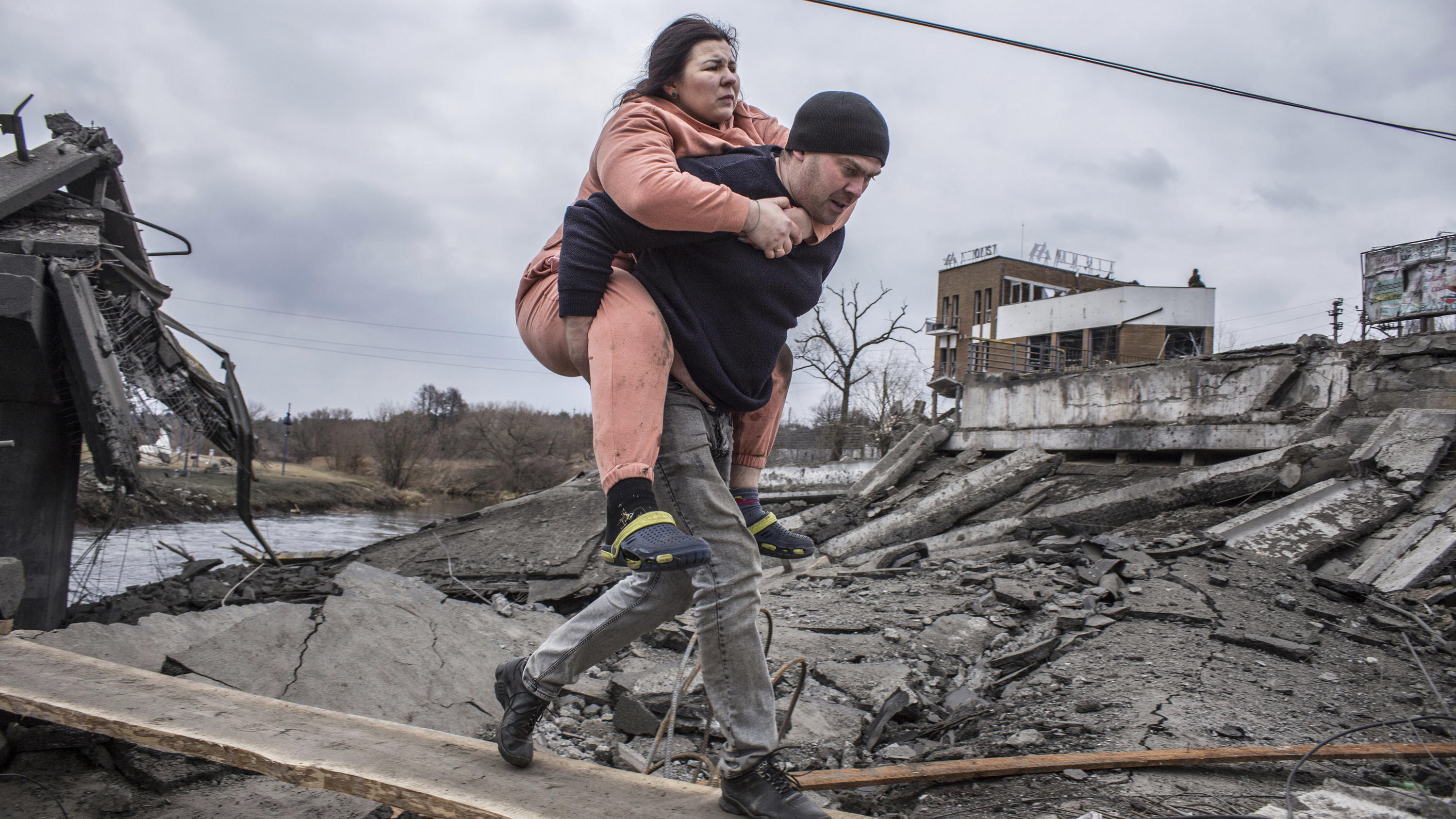 dpatopbilder - 06.03.2022, Ukraine, Irpin: Ein Mann trägt eine Frau, als sie auf der Flucht aus der Stadt Irpin einen improvisierten Weg zwischen Trümmern überqueren. Foto: Oleksandr Ratushniak/AP/dpa +++ dpa-Bildfunk +++