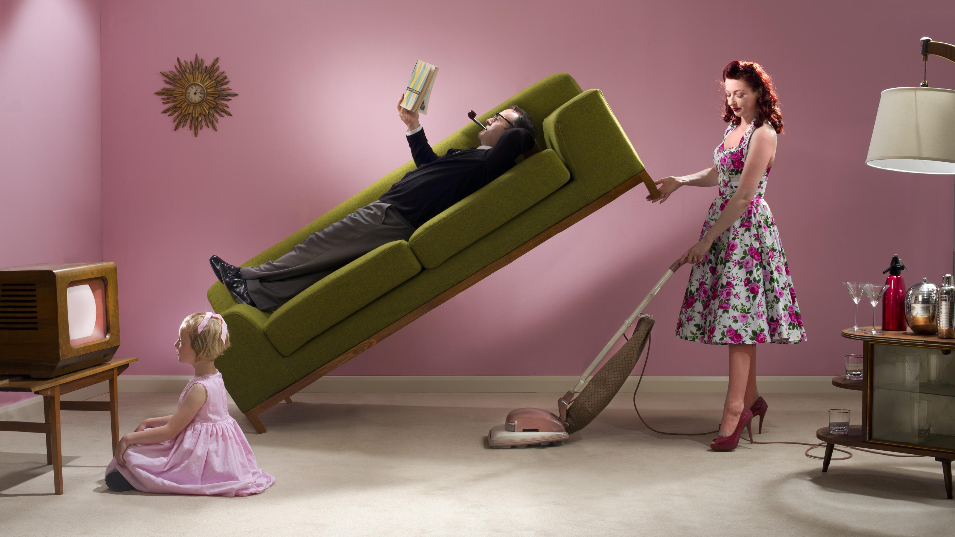 Ein Retro-Darstellung der klassischen Rollenverteilung innerhalb einer Familie. Der Mann liegt auf der Couch, während die Frau staubsaugt.