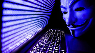 Binärcode auf Laptop und Guy Fawkes-Maske davor; das Cyber-Kollektiv Anonymous hat Russland den Cyberkrieg erklärt
