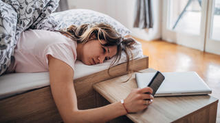 Müde Frau im Bett mit Handy