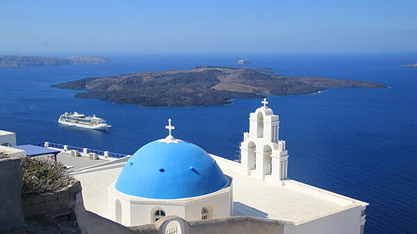 Blick auf eine Kirche mit blauem Kuppeldach auf der griechischen Ferieninsel Santorini.