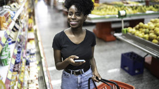 Frau mit Korb und Handy in der Hand im Supermarkt