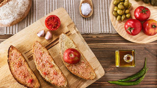Two slices of bread with tomato pulp and olive oil , one slice with half ramillet tomato and the rest of the ingredients like garlic, typical "ramillet" tomatoes from Mallorca, oil bottle, green olives and pickles. All distributed on a dark brown wooden table.