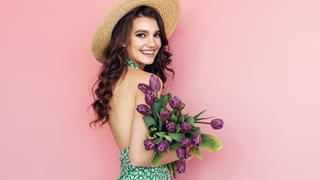 Frau im sommerlichen Kleid hält ein Strauß Tulpen im Arm.