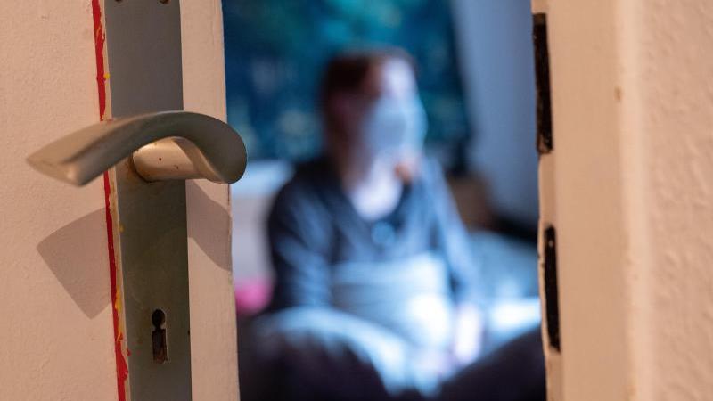 Eine Frau sitzt während der Isolation nach einem positiven Corona-PCR-Test auf ihrem Bett. Foto: Sebastian Gollnow/dpa/Symbolbild