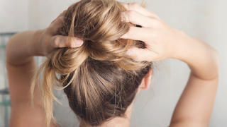 Eine junge Frau steht vor ihrem Badezimmerspiegel und stylt sich ihre langen Haare.
