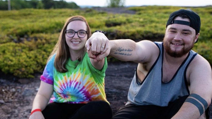 Aaron und Kayla halten ihre Eheringe ins Bild.