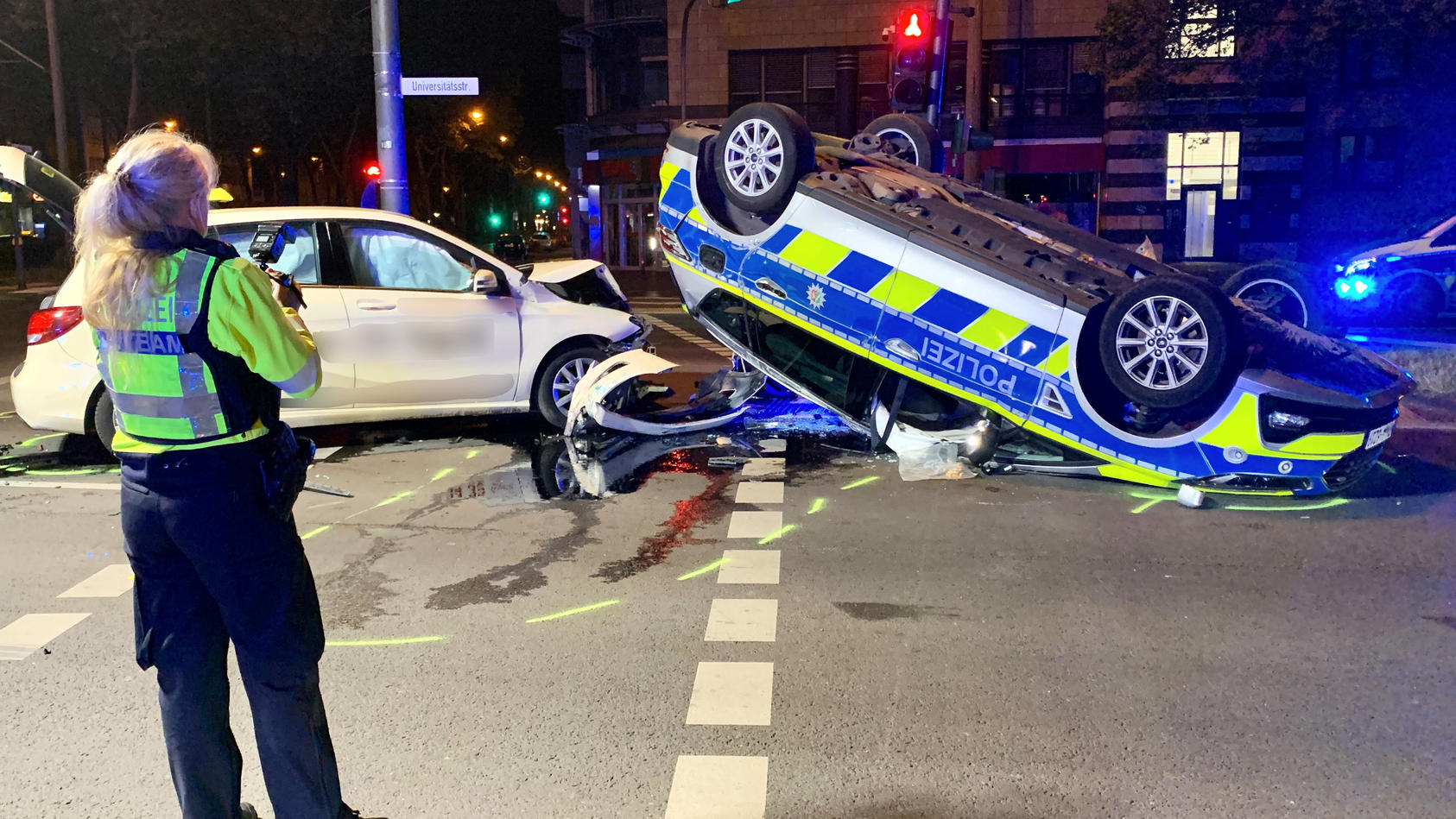 07.05.2022, Nordrhein-Westfalen, Köln: Eine polizistin betrachtet die Unfallstelle. Auf dem Weg zu einem Einsatz ist ein Streifenwagen in Köln in der Nacht auf Samstag mit einem Taxi kollidiert  - dabei sind sechs Menschen verletzt worden. Wie ein Sp