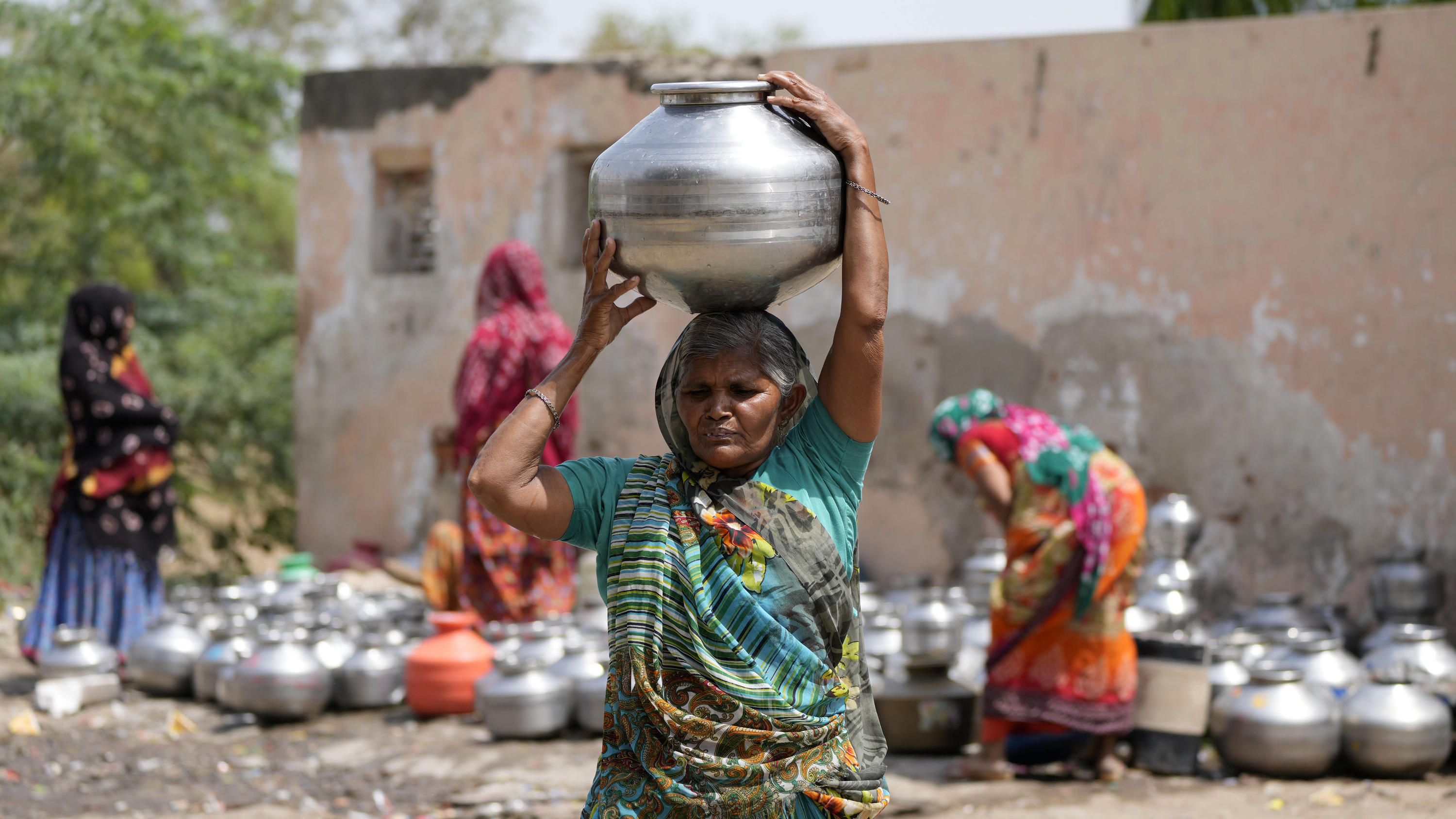 10.05.2022, Indien, Ahmedabad: Eine Frau aus einem Slum trägt einen Wasserkrug auf den Kopf, in dem sich Trinkwasser aus einem Brunnen einer Tempelanlage befindet. Foto: Ajit Solanki/AP/dpa +++ dpa-Bildfunk +++