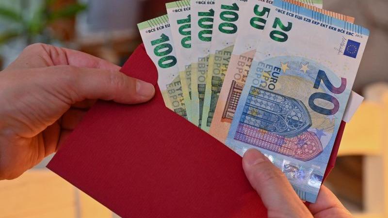 eine-frau-steckt-eurobanknoten-in-einen-umschlag-foto-patrick-pleuldpa-zentralbilddpaillustration