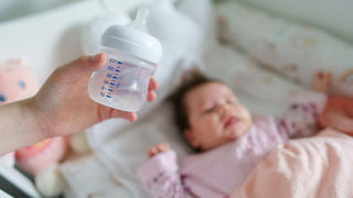 Mutter hält leere Babyflasche vor Säugling