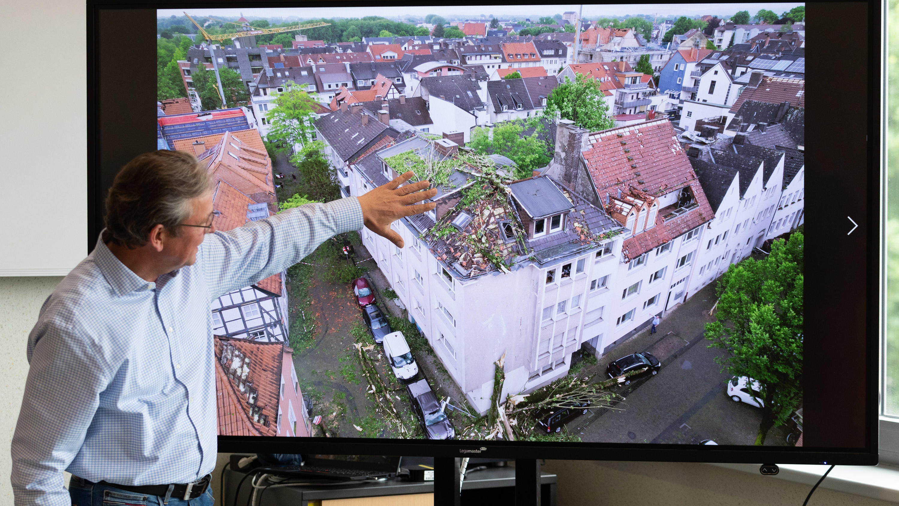 21.05.2022, Nordrhein-Westfalen, Paderborn: Der Bürgermeister von Paderborn, Michael Dreier, spricht bei einer Pressekonferenz vor einem Display mit einem Schadensbild aus der Innenstadt, das zeigt wie Bäume auf ein Hausdach geweht worden sind. Ein T