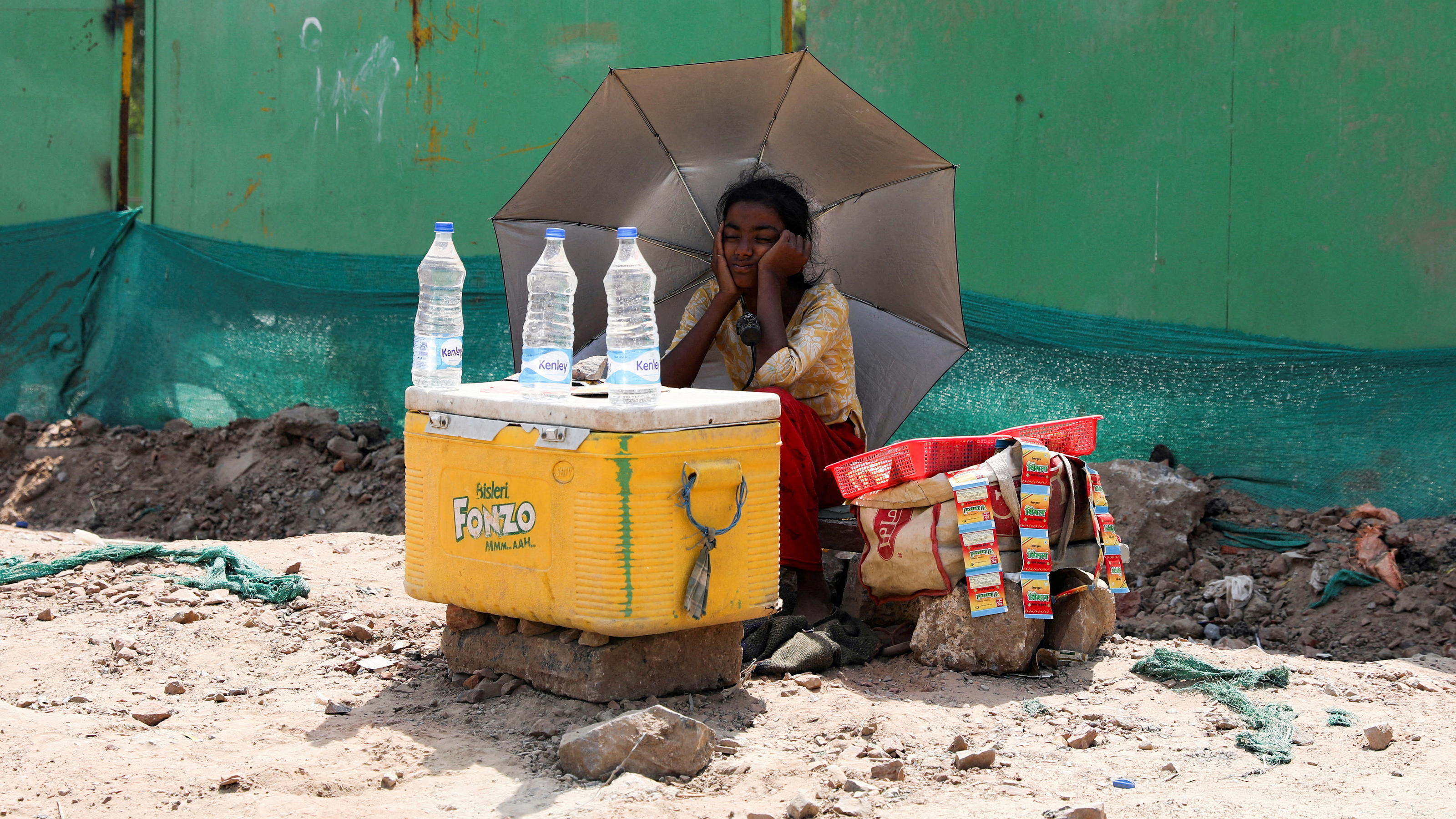FILE PHOTO: A girl selling water uses an umbrella to protect herself from the sun as she waits for customers on a hot summer day, in New Delhi, India, April 27, 2022. REUTERS/Anushree Fadnavis/File Photo