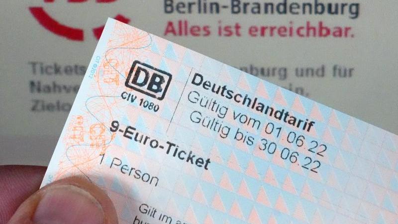 Ein Ausgedrucktes 9-Euro-Ticket in der Hand eines Mannes vor dem Logo des Verkehrsverbundes Berlin-Brandenburg