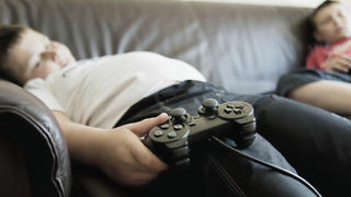 Kind liegt auf Couch und spielt an Spielekonsole