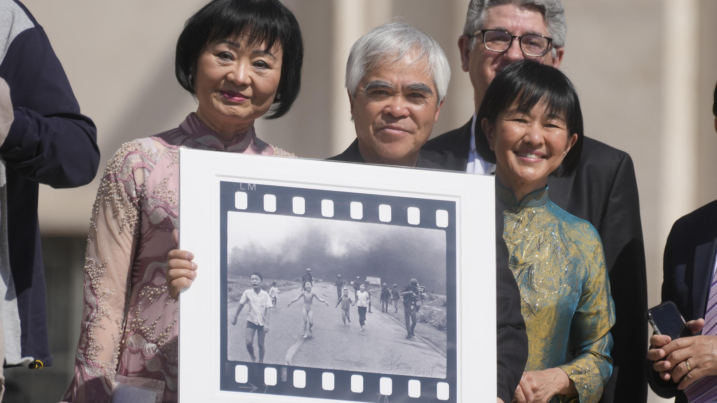 ARCHIV - 11.05.2022, Vatikan, Vatikanstadt: Der vietnamesisch-amerikanische Fotograf Nick Ut (M), hält sein mit dem Pulitzer-Preis ausgezeichnetes Foto «Napalm Girl», flankiert von Phan Thi Kim Phuc (l), die auf diesem Foto abgebildet ist, während si