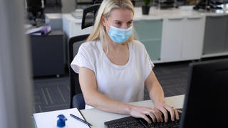 Frau im Büro mit Maske am Computer