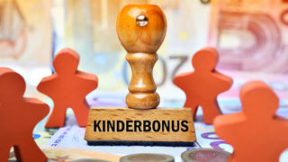 FOTOMONTAGE, Stempel mit Aufschrift Kinderbonus und Kinderfiguren auf Geldscheinen