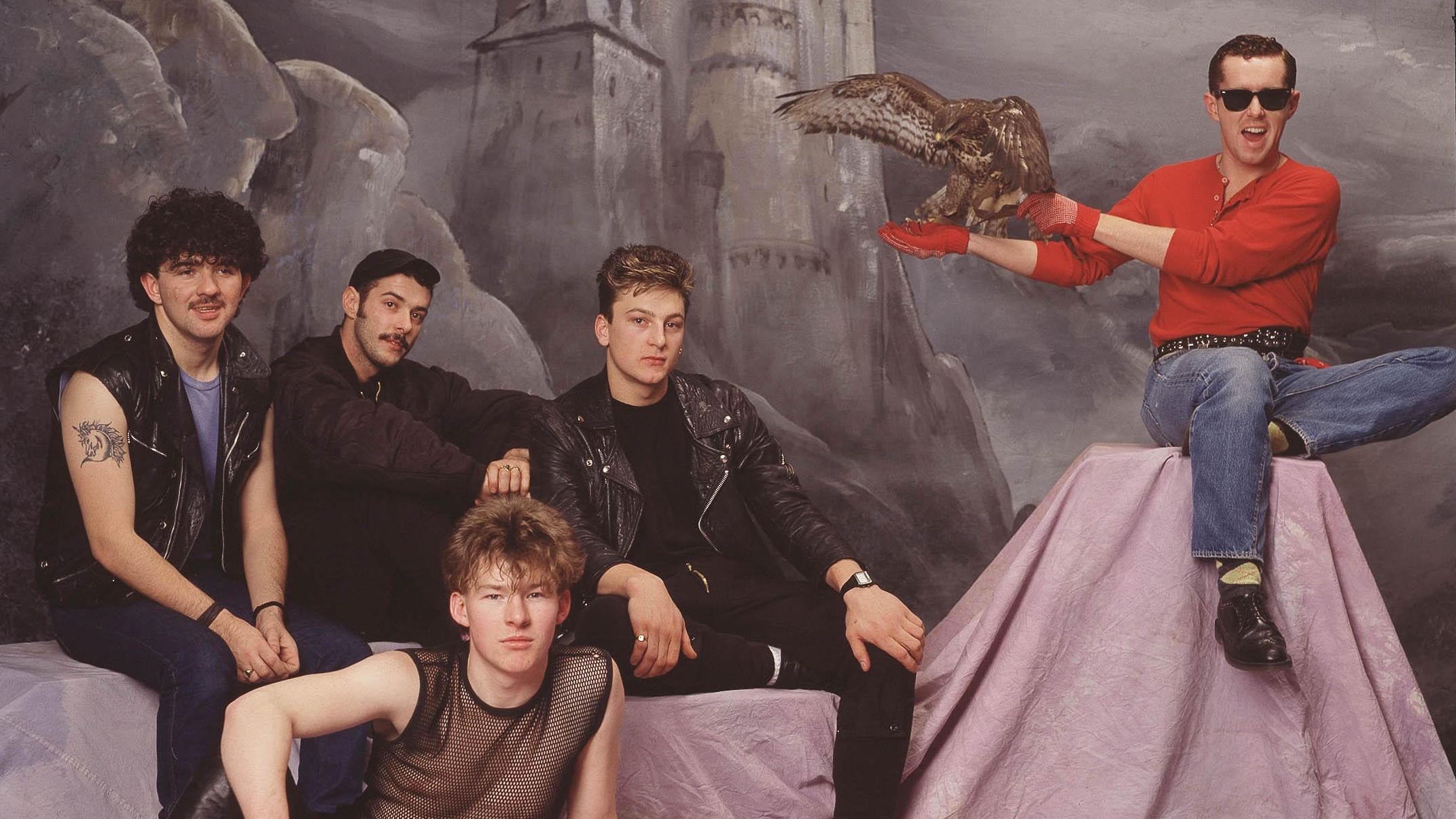 Portrait der Band Franky goes to Hollywood aus dem Jahr 1984. Eines der Bandmitglieder trägt einen Raubvogel auf dem Arm, währenddessen die anderen Bandmitglieder in verrückten Outfits die Kamera schauen