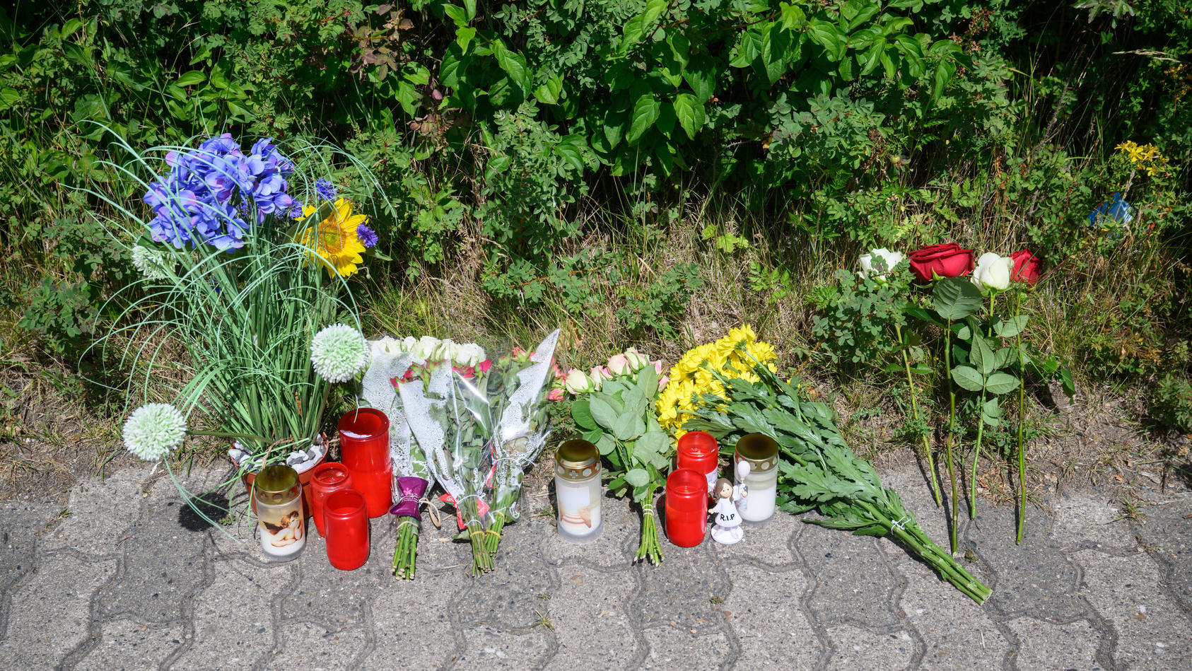 22.06.2022, Niedersachsen, Salzgitter: Kerzen, Blumen und Figuren zum Gedenken an eine getötete 15-jährige liegen an einem Tatort an einer Grünfläche am Hans-Böckler-Ring. Nach dem Fund einer toten 15-Jährigen in Salzgitter gelten zwei Jugendliche al