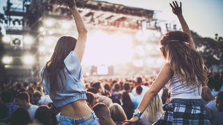 Zwei Frauen die auf einem Konzert auf den Schultern anderer Personen sitzen.
