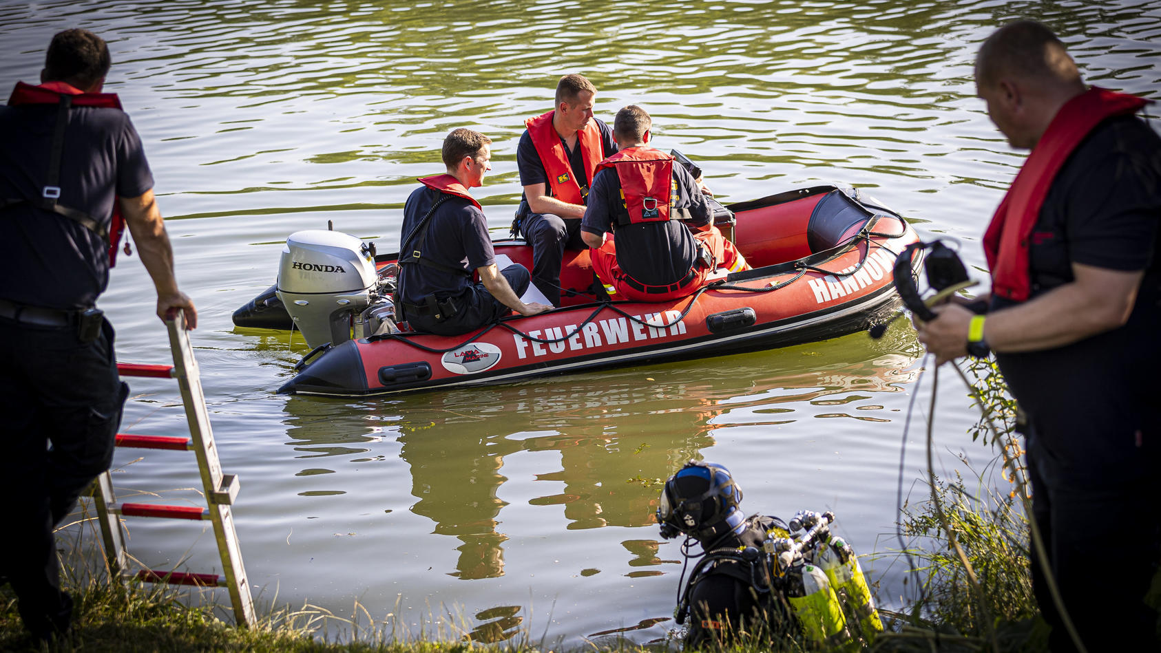 30.06.2022, Niedersachsen, Hannover: Einsatzkräfte sind in einem Boot im Wasser vom Dreiecksteich unterwegs. In dem Baggersee ist ein Mann ertrunken. Foto: Moritz Frankenberg/dpa +++ dpa-Bildfunk +++