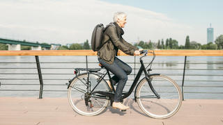 Ältere Frau fährt Fahrrad am Fluss entlang