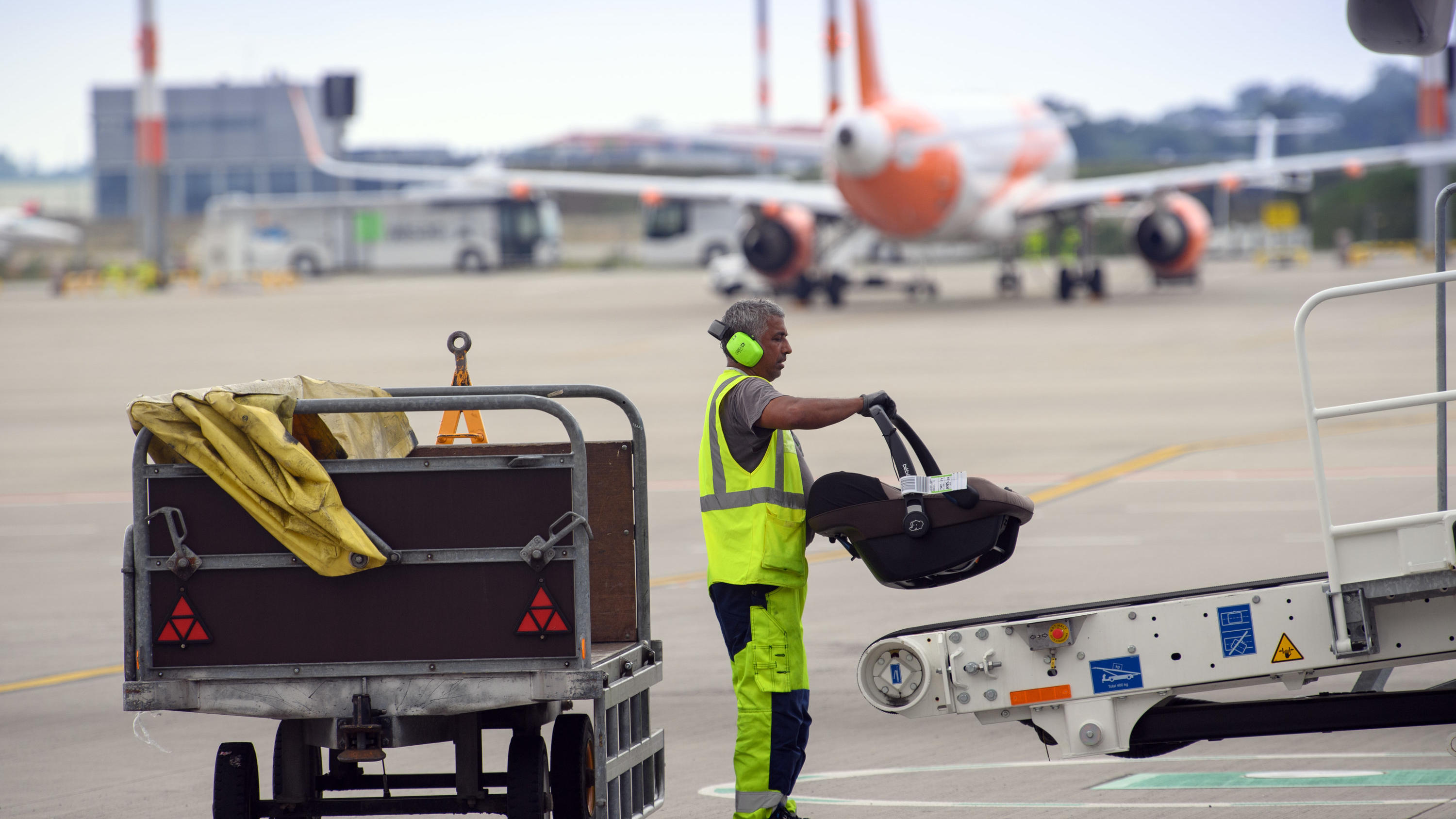 Brandenburg, Schönefeld: Ein Mitarbeiter der WISAG Aviation lädt auf dem Vorfeld des Flughafen BER ·Willy Brandt· einen Kindersitz auf das Gepäck-Transportband