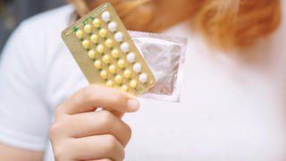 Frau hält Pille und Kondom in den Händen.
