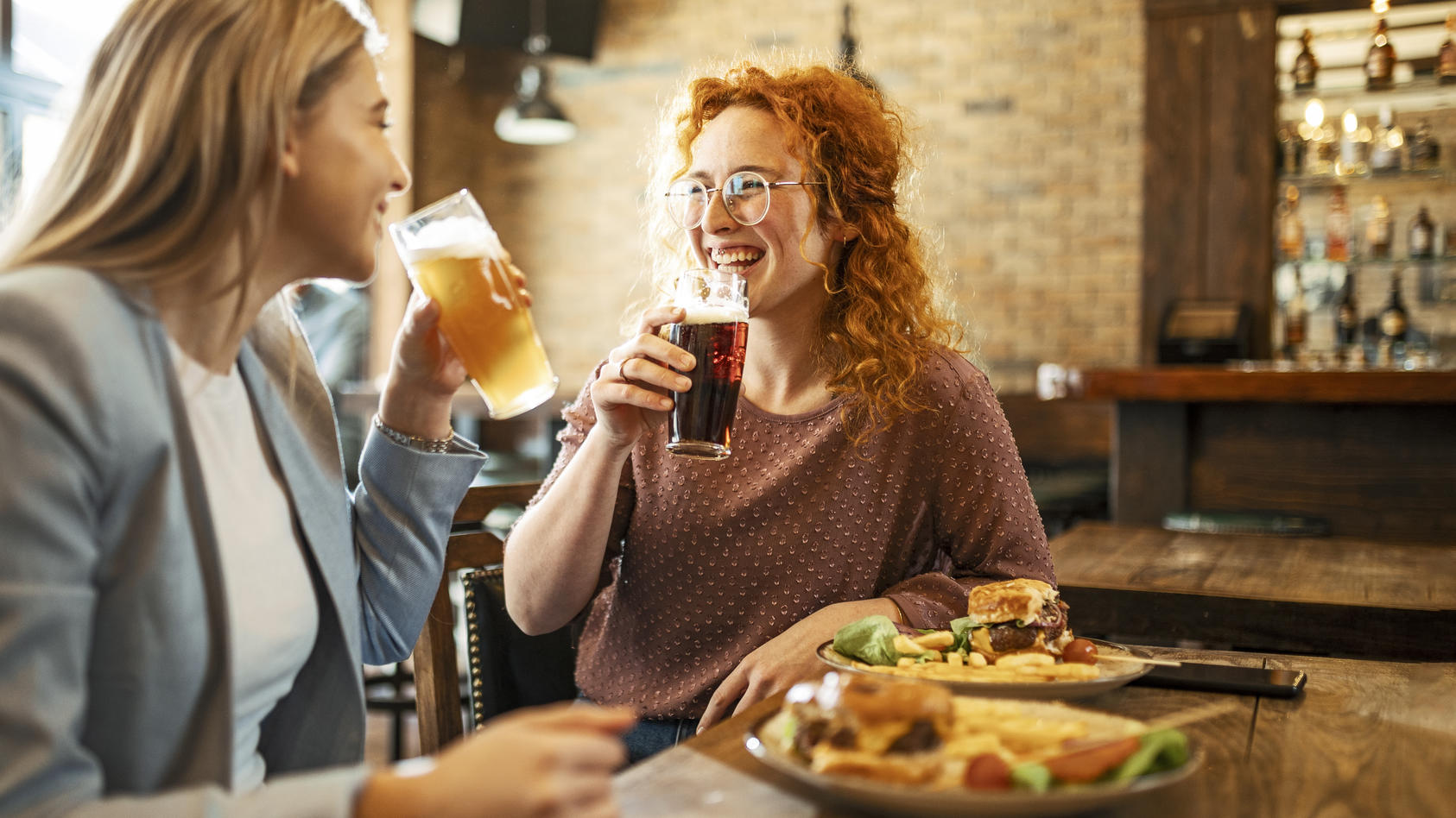Zwei Freundinnen sitzen im Restaurant und trinken Bier und essen einen Burger.
