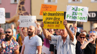 28.07.2022, Bayern, Bayreuth: Demonstranten halten während des Bürgerdialogs von Bundeswirtschaftsminister Habeck im Ehrenhof der Stadt hinter einer Absperrung Plakate mit der Aufschrift ·Ja zum Frieden·, ·Verräter· oder ·Wir demonstrieren gegen diese Klimapolitik! Mach mit·. Es gab zudem laute Pfiffe und Buhrufe, viele Bürger riefen Habeck zu: «Hau ab». Foto: Soeren Stache/dpa +++ dpa-Bildfunk +++