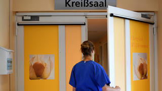 ARCHIV - 12.07.2018, Berlin: Eine Mitarbeiterin steht vor einem Kreißsaal in einem Krankenhaus. (zu dpa: «Kassen: Zahl der Kaiserschnitt-Geburten leicht gestiegen») Foto: Britta Pedersen/dpa-Zentralbild/dpa +++ dpa-Bildfunk +++