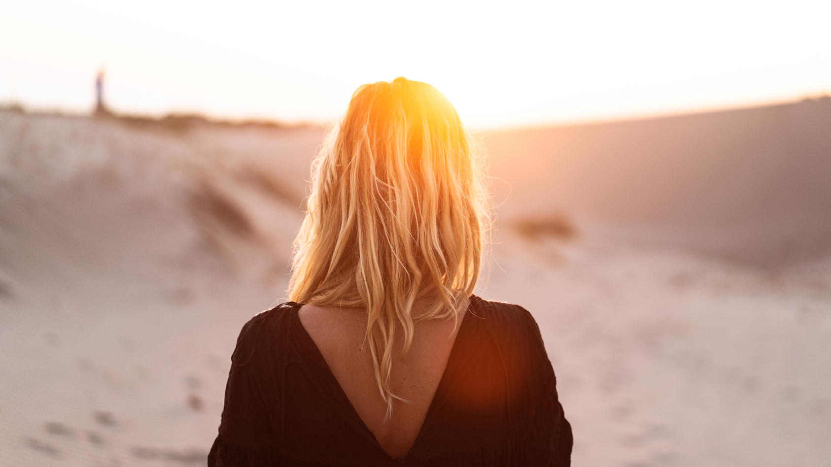 Was macht die Sonne mit unseren Haaren? Eine Frau läuft am Strand entlang.
